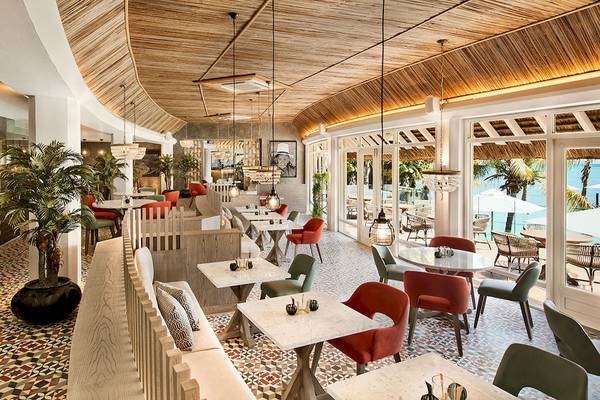 Innenansicht des Restaurants im LUX Grand Gaube Resort & Villas mit bunten Stühlen und Tischen, bepflanzten Ecken und Blick auf den Ozean.