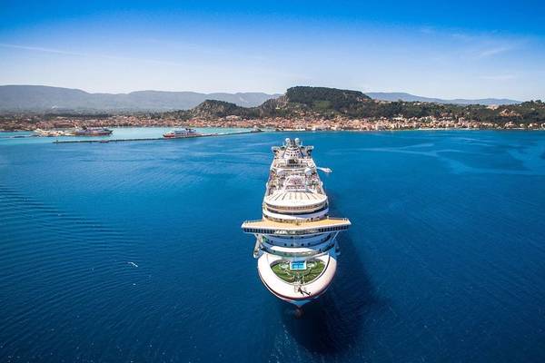 Ein Kreuzfahrtschiff des Galaxy Beach Resorts fährt in den Hafen ein, mit Bergen und Gebäuden im Hintergrund.