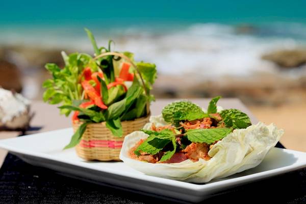 Ein Teller mit einem Thai-Gericht, umgeben von Meeresfrüchten, serviert auf einem weißen Teller am Strand im Moracea by Khao Lak Resort.