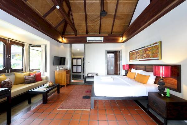 Innenansicht eines Hotelzimmers im Moracea by Khao Lak Resort mit einem großen Bett, Couch, Tisch und Fernseher.