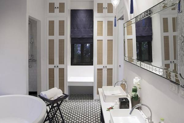 Innenansicht des Badezimmers im Moracea by Khao Lak Resort mit weißen Wänden, schwarzen und weißen Fliesenboden, zwei Waschbecken und einem großen Spiegel.