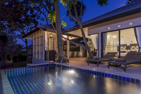 Nachtansicht der Villa im Moracea by Khao Lak Resort mit Swimmingpool und Loungestühlen.