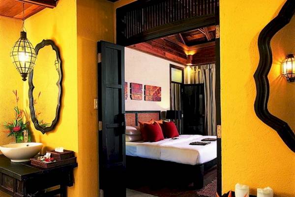 Innenansicht eines Zimmers im Moracea by Khao Lak Resort mit gelben Wänden, einem Bett, einem Waschbecken und einem Spiegel.