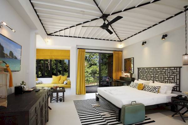Schlafzimmer im Moracea by Khao Lak Resort mit weißem Bett, gelben Kissen und schwarzen Vorhängen.