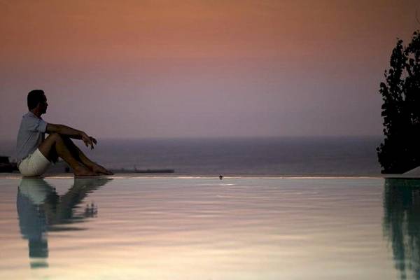 Mann sitzt am Poolrand und genießt den Sonnenuntergang am Meer.