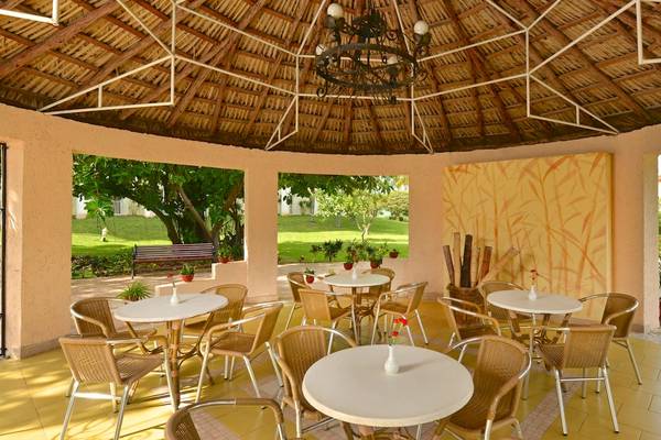 Gartenterrasse des Iberostar Tainos Hotels mit Tischen und Stühlen, gelber Wand und Blick auf die Landschaft.