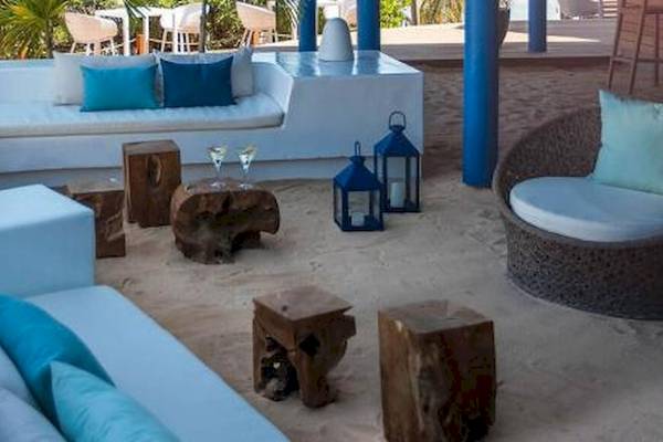 Loungebereich des Veranda Pointe Aux Biches Hotels mit weißen Möbeln und blauen Kissen auf Sand.