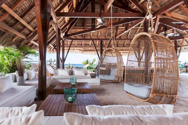 Loungebereich im Freien im Veranda Pointe Aux Biches Hotel mit weißen Möbeln, hängenden Körben und Blick auf das Meer.