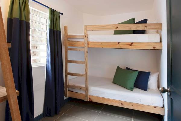 Doppel-Stockbett im Zimmer des Veranda Pointe Aux Biches Hotels mit grünen und blauen Kissen und weißen Laken.