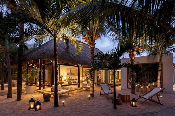 Nachtansicht des Veranda Pointe Aux Biches Hotels mit Palmen und Laternen auf dem Sand.