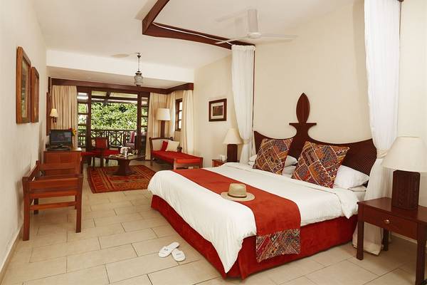 Innenansicht des Hotelzimmers im Neptune Beach Resort in Kenia, mit einem großen Bett, Tisch, Stühlen und Fernseher.