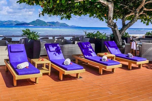 Terrasse des La Digue Island Lodge mit mehreren Liegen und Blick auf das Meer.