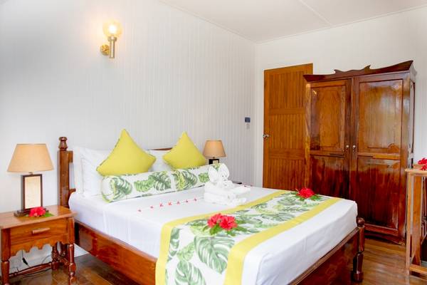 Schlafzimmer im La Digue Island Lodge mit einem Bett, gelben Kissen, Blumen und Holzmöbeln.