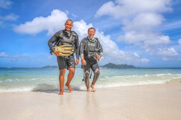 Zwei Taucher am Strand von La Digue Island Lodge, bereit für eine Unterwasserabenteuer.