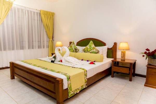 Schlafzimmer im La Digue Island Lodge mit einem Bett, zwei Nachttischen, rosa Rosen und gelben Vorhängen.