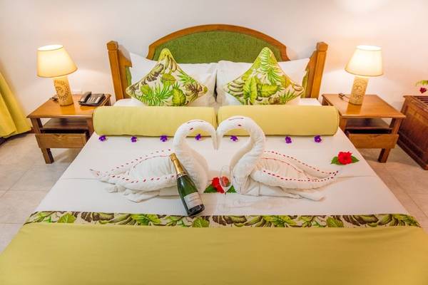 Ein Bett im La Digue Island Lodge mit zwei Schwanen und Champagnerflasche.