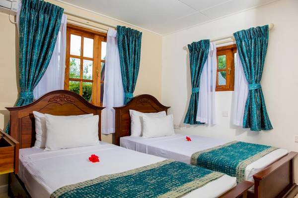 Doppelbett-Zimmer im La Digue Island Lodge mit blauen Vorhängen und weißen Laken.