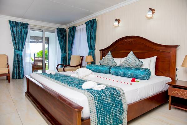 Ein elegantes Zimmer im La Digue Island Lodge mit einem großen Bett, blauen Vorhängen und einem Ausblick auf eine Terrasse.