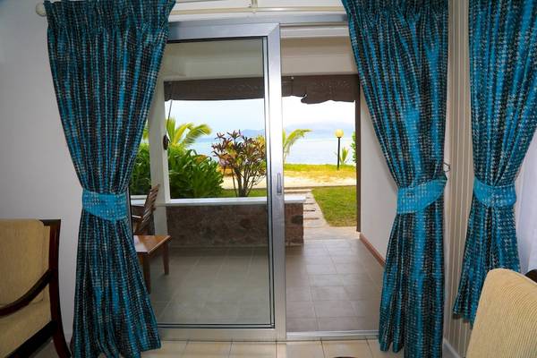 Blick aus dem Zimmer des La Digue Island Lodge mit blauen Vorhängen und einem Ausblick auf das Meer.