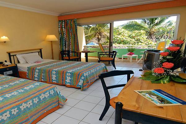 Doppelzimmer im Brisas del Caribe Hotel mit zwei Betten, Tisch, Fernseher und Balkonzugang.