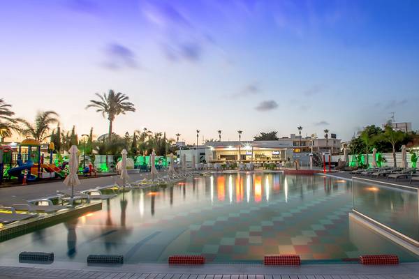 Der Swimmingpool des Nicholas Color Hotels bei Dämmerung mit Loungeliegen und bunten Lichtern.
