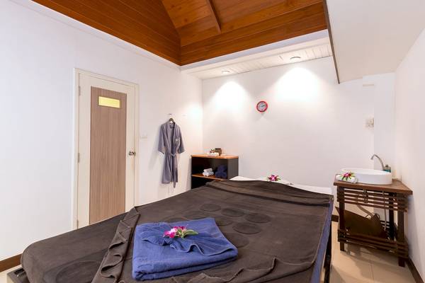 Massageraum im Best Western Premier Bangtao Beach Resort mit Bett, blauen Handtüchern und Waschbecken.