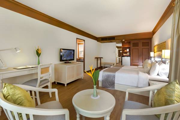 Hotelzimmer im Best Western Premier Bangtao Beach Resort mit Schreibtisch, Stühlen, Bett, Fernseher und Blumenvase.
