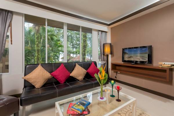 Wohnzimmer im Best Western Premier Bangtao Beach Resort mit schwarzem Sofa, Fenstern und Fernseher.