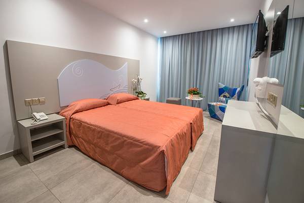 Doppelbett in einem Zimmer im Nicholas Color Hotel mit grauem Kopfteil, orangem Bettlaken und Tisch neben dem Bett.