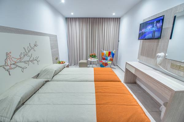 Doppelzimmer im Nicholas Color Hotel mit zwei Betten, buntem Stuhl und Fernseher.