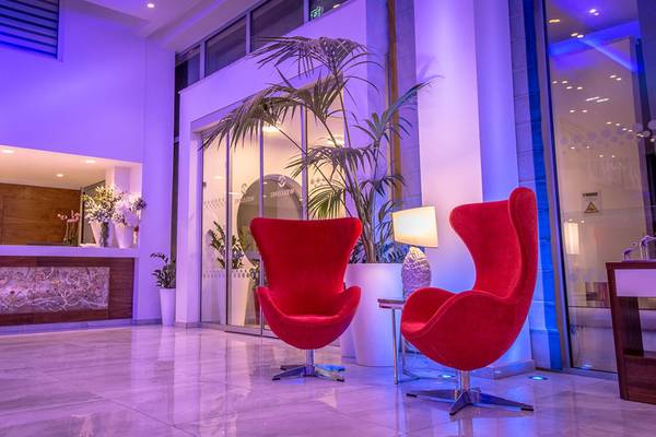 Hotellobby mit zwei roten Sesseln, violetter Beleuchtung und Pflanzen im Hintergrund.