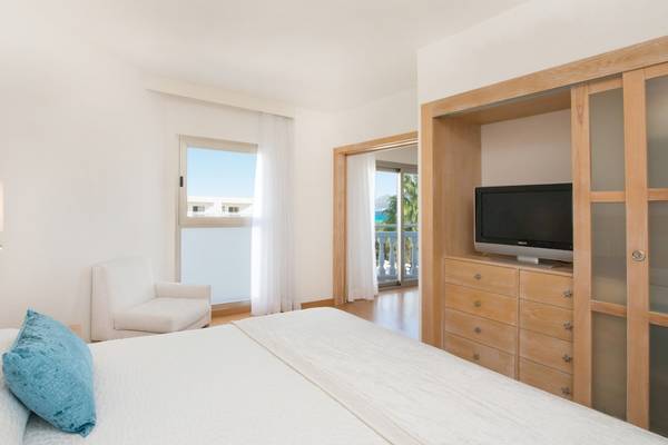 Innenansicht eines modernen Hotelzimmers mit Bett, Fernseher, Schrank und Balkon.