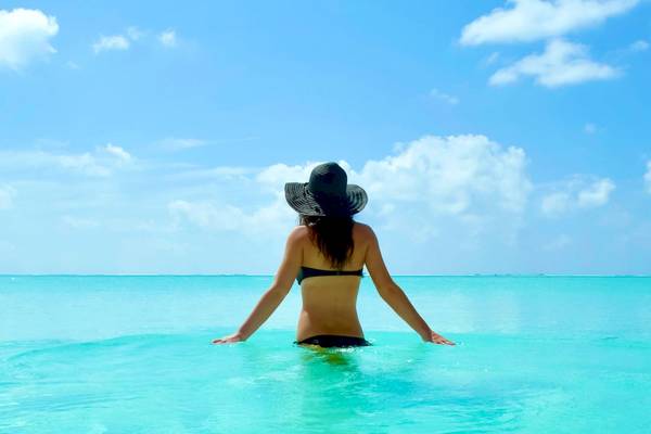 Frau mit schwarzem Hut im Wasser vor einem Hotel in den Malediven