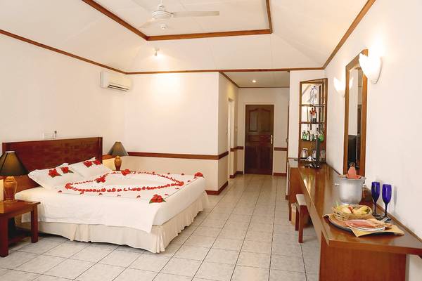 Schlafzimmer der Villa Park, Malediven, mit Bett, Blumendekoration, Tisch und Minibar.
