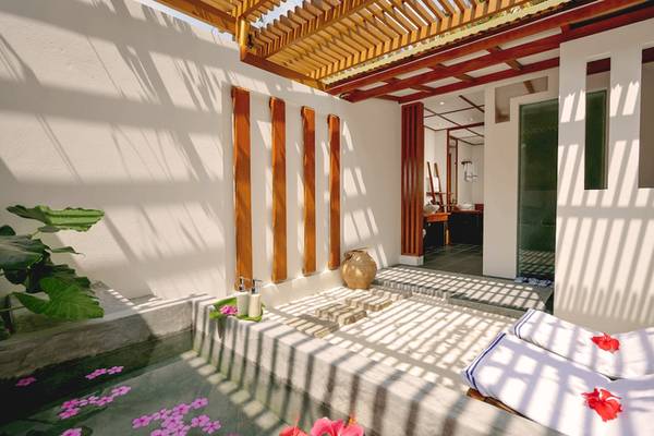 Außenbereich des Villa Park in den Malediven mit Pool, Blumen und Liegen.