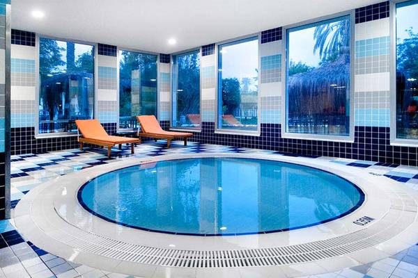Innenansicht des Schwimmbeckens im Belconti Resort mit blauen und weißen Fliesen und zwei orange Liegestühlen.
