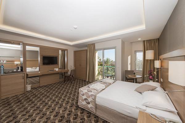 Innenansicht eines Hotelzimmers im Belconti Resort mit Bett, Fernseher, Schreibtisch und Balkon.