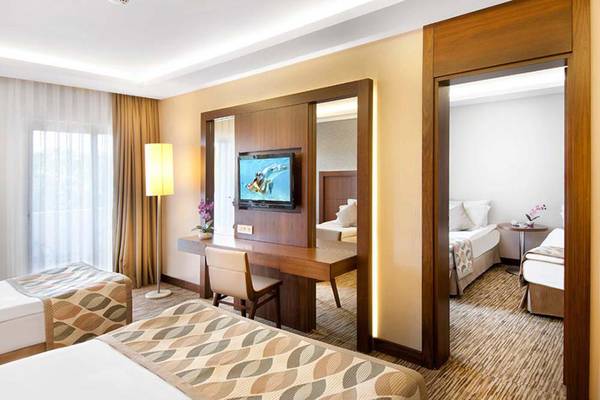Innenansicht eines Hotelzimmers im Belconti Resort mit Fernseher, Schreibtisch und zwei Betten.