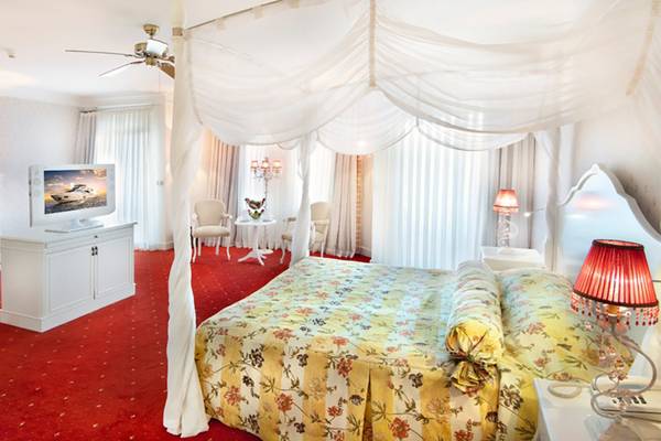 Schlafzimmer im Belconti Resort mit vierposterbett, roter Teppich und Fernseher.
