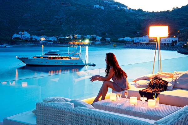 Eine Frau sitzt am Pool und blickt auf das Meer, ein Boot im Hintergrund