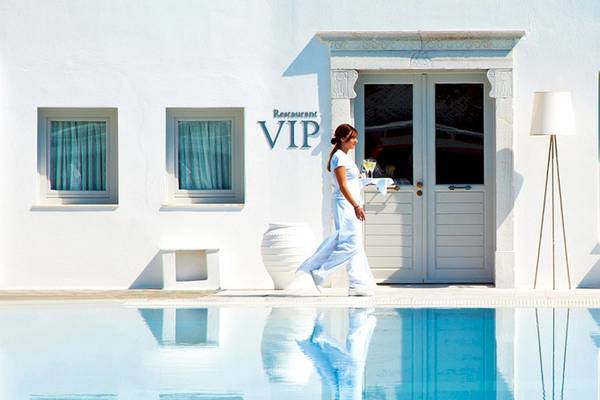 Frau in einem weißen Kleid, die vor einem weißen Hotel namens VIP steht und einen Cocktail serviert.