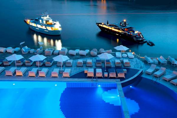 Poolbereich des Petasos Beach Resort & Spa mit beleuchteten Liegestühlen und Yachten bei Nacht
