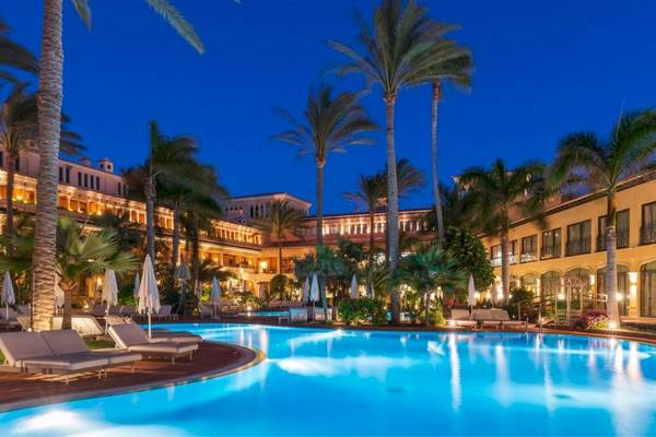 Nachtansicht des Swimmingpools des Secrets Bahia Real Resort & Spa mit Loungeliegen und Palmen