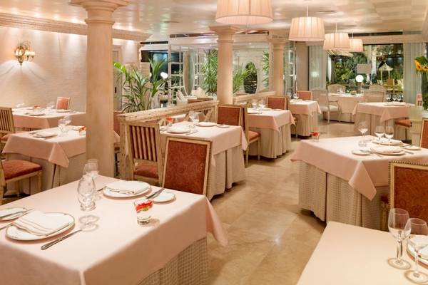 Innenansicht des Restaurants des Secrets Bahia Real Resort & Spa mit gedeckten Tischen, eleganten Stühlen und beleuchteten Kronleuchtern.