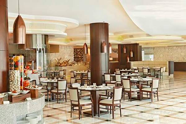 Innenansicht des Restaurants im Waldorf Astoria Dubai Palm Jumeirah mit gepolsterten Stühlen, Holztischen und dekorativen Kronleuchtern.