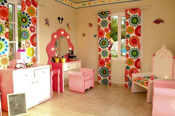 Ein Kinderzimmer mit rosa Möbeln und bunter Blumentapete an den Wänden.