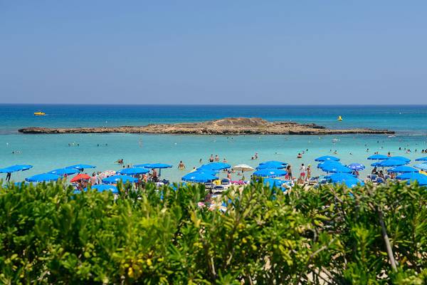 Ausblick auf den Strand mit vielen Gästen und blauen Sonnenschirmen am Capo Bay Hotel