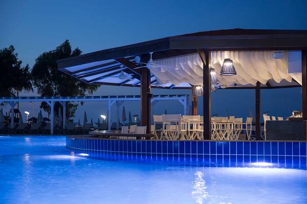 Der Poolbereich des Capo Bay Hotels bei Nacht mit beleuchteter Überdachung und Tischen und Stühlen.