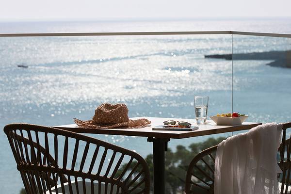 Aussicht vom Balkon des Capo Bay Hotels mit Meerblick, Strohhut, Buch, Sonnenbrille und Obstschüssel.