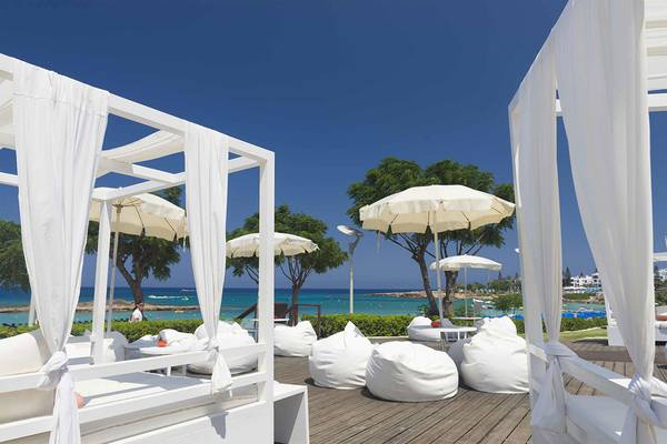 Loungebereich des Capo Bay Hotels mit weißen Sonnenschirmen und Loungestühlen am Meer